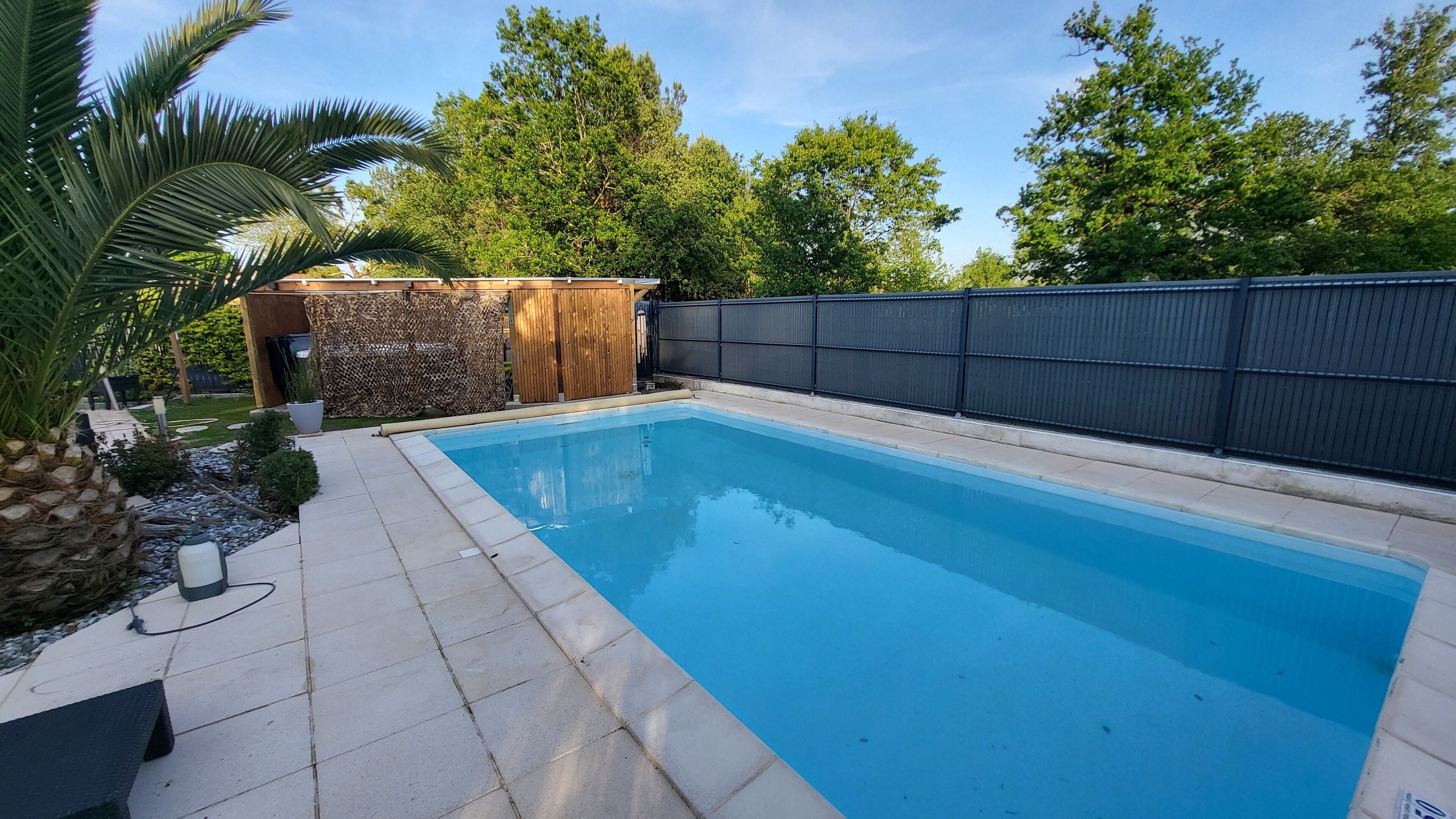 Una piscina rettangolare con bordo piastrellato, circondata da un muro in pietra e una recinzione in legno.
