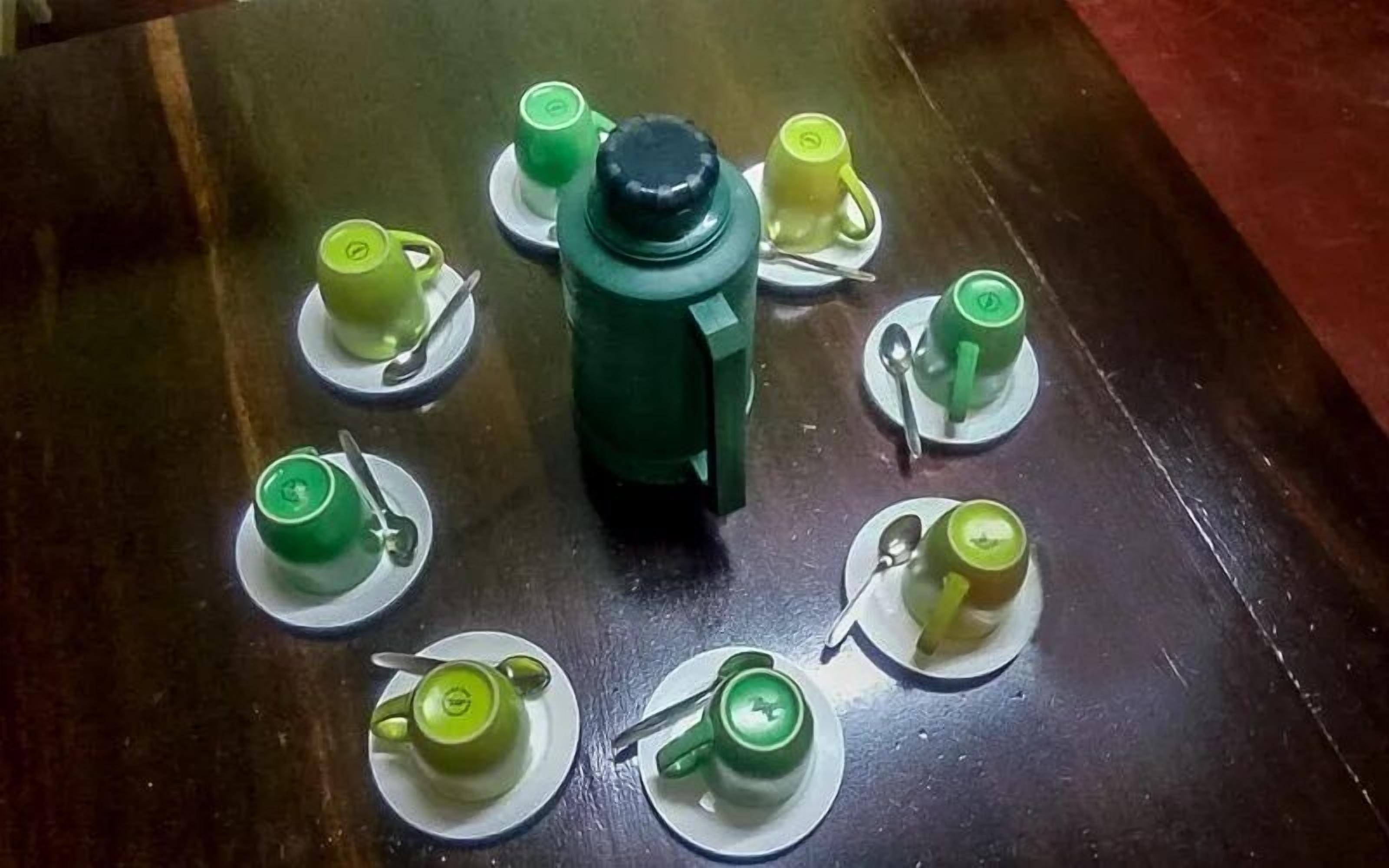 Ein Tisch mit einem zentral platzierten grünen Objekt, umgeben von acht grünen Tassen und Untertassen.