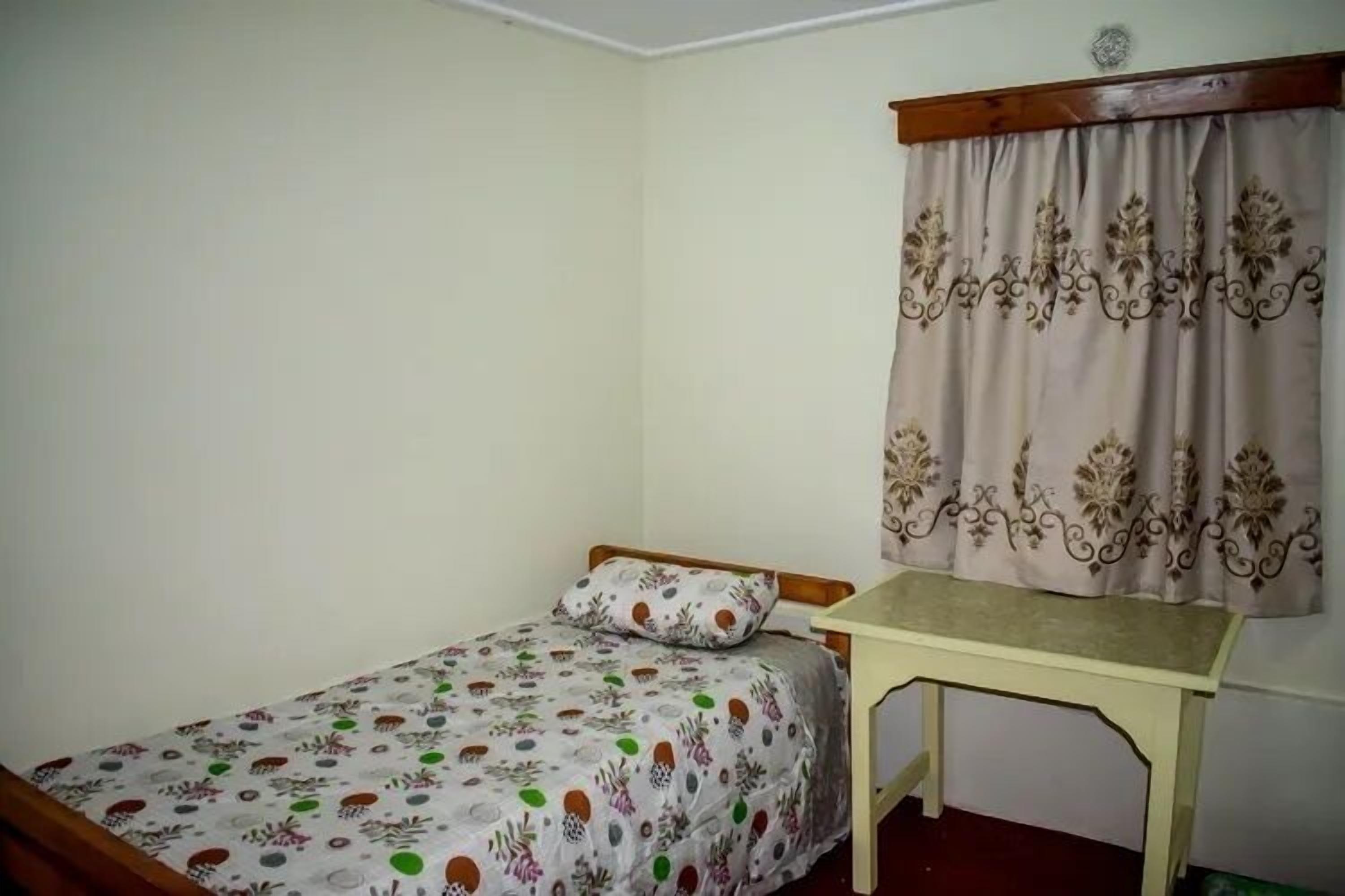 Una habitación pequeña con una cama individual, cabecera de madera, mesita de noche y colcha estampada.
