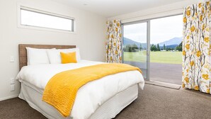 Un dormitorio con una cama grande, vista a un campo verde y una montaña al fondo.