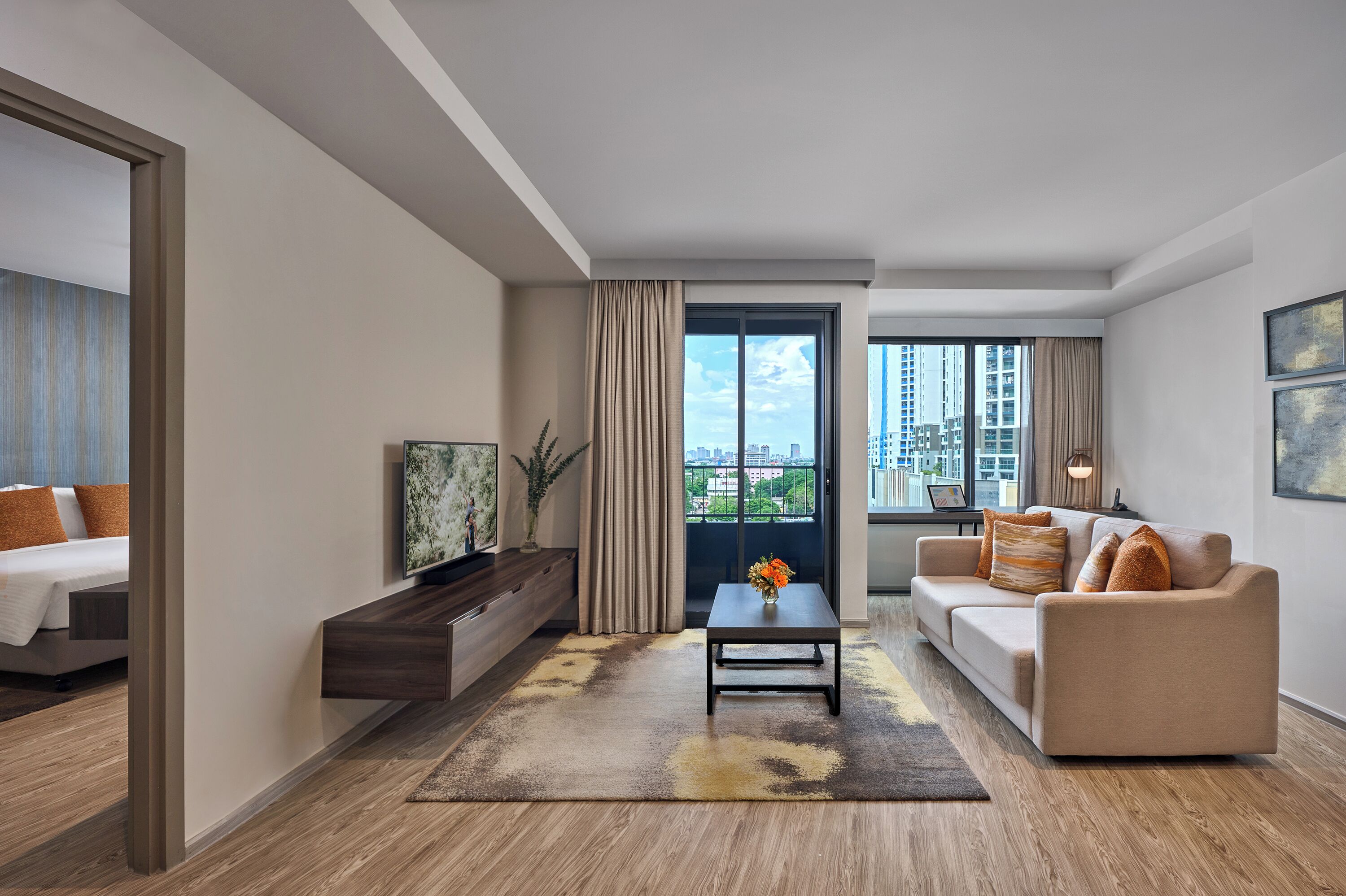 Une chambre d’hôtel moderne équipée d’un canapé, d’une table basse, d’un téléviseur et d’une grande fenêtre donnant sur la ville.