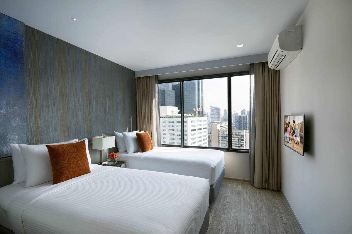 Une chambre d’hôtel avec deux lits, une grande fenêtre donnant sur la ville, un téléviseur à écran plat et un système de climatisation.