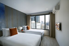 A hotel room with two beds, a large window with a city view, a flat-screen TV, and an air conditioning unit.