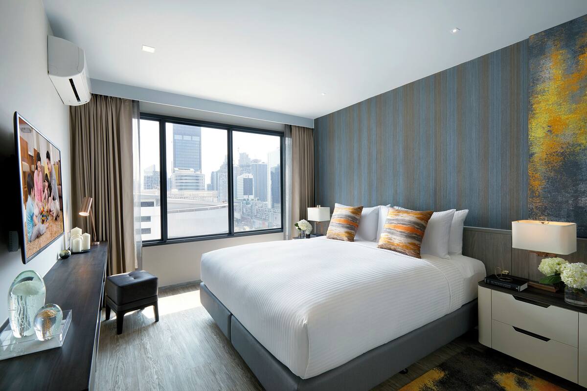 Une chambre d’hôtel moderne dotée d’un grand lit, d’une table de chevet, d’un bureau et d’une grande fenêtre donnant sur la ville.