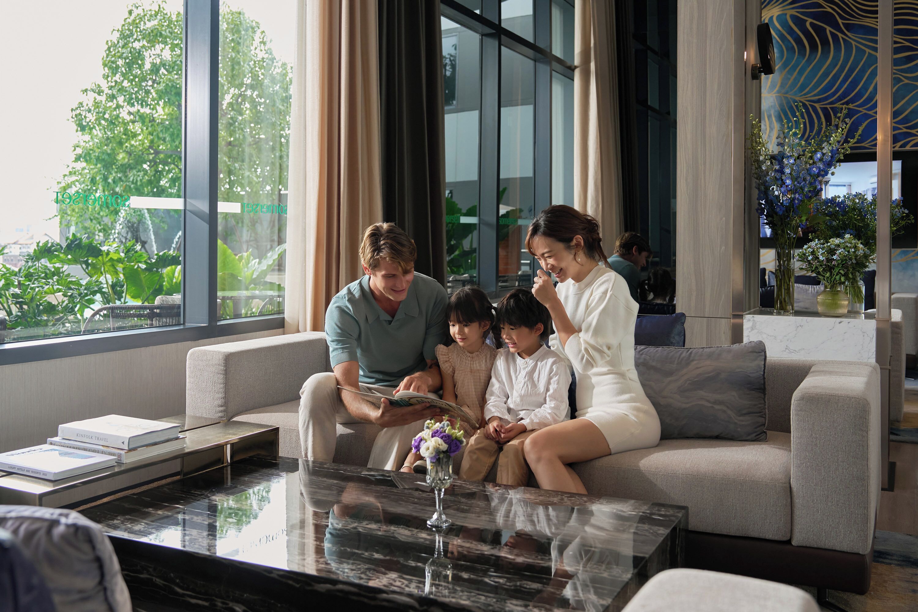 A family sitting on a sofa with a view of greenery outside.