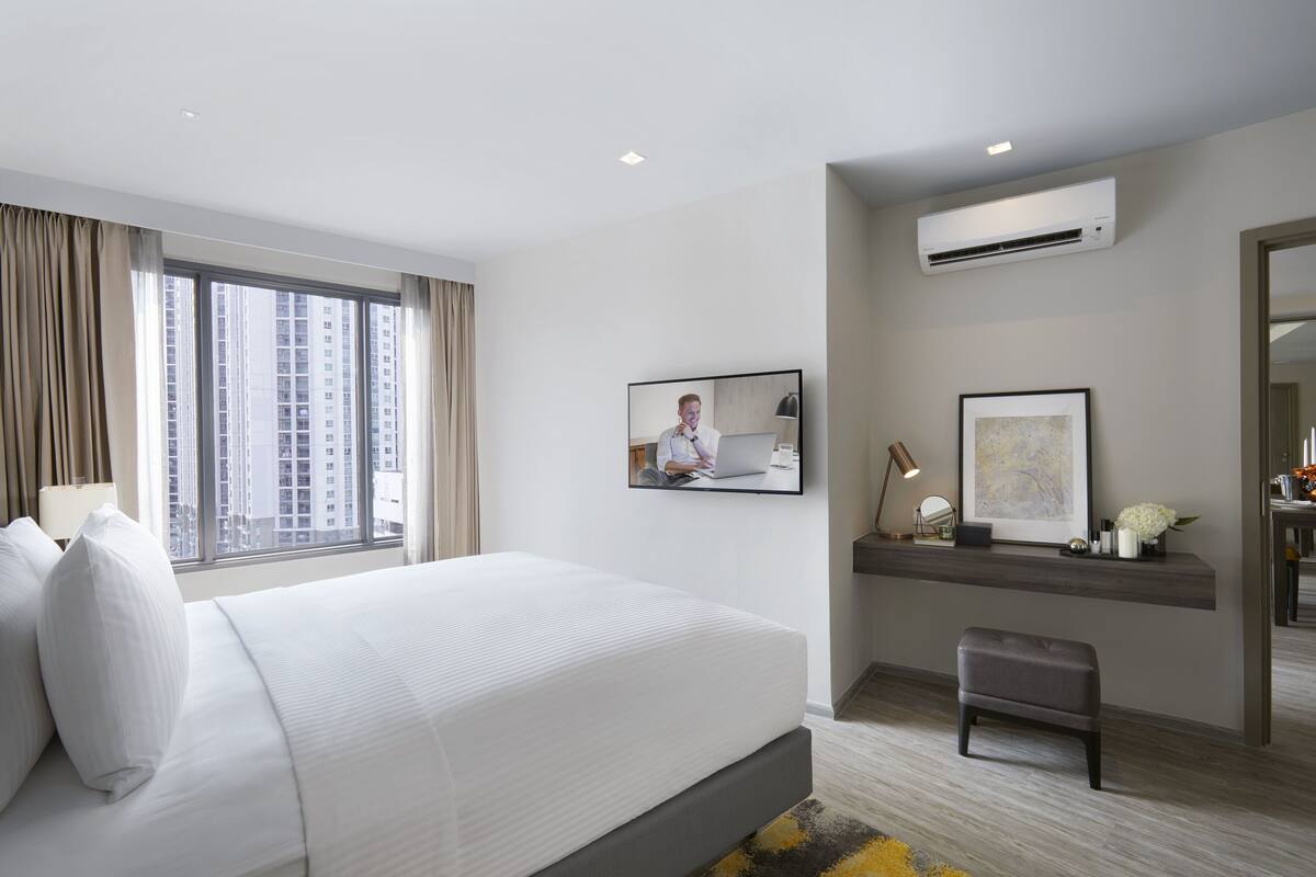 Une chambre d’hôtel moderne dotée d’un grand lit, d’un bureau avec un ordinateur, d’un téléviseur fixé au mur et d’un appareil de climatisation.