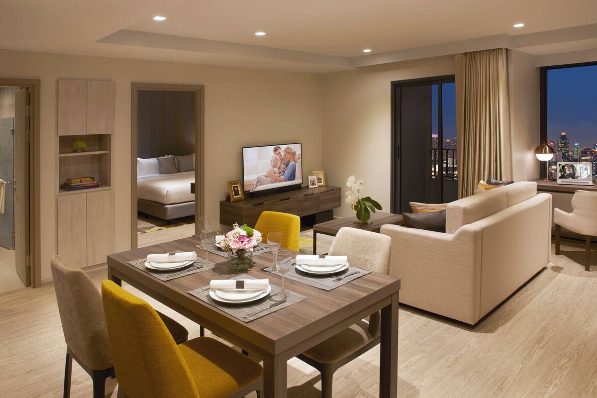Une chambre d’hôtel moderne dotée d’un coin repas, d’un canapé, d’une télévision et offrant une vue sur la ville.