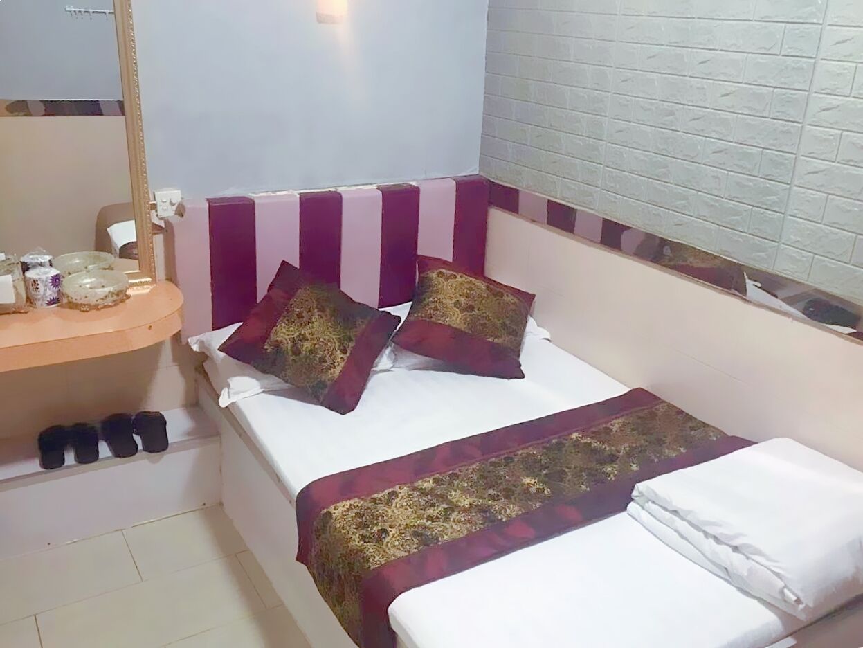 A hotel room with a bed, a small bedside table, and a mirror.