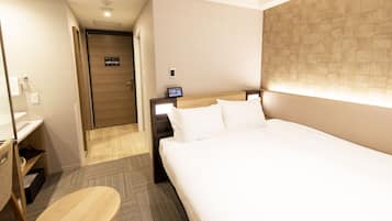 A hotel room with a bed, bedside table, and a small desk with a chair.