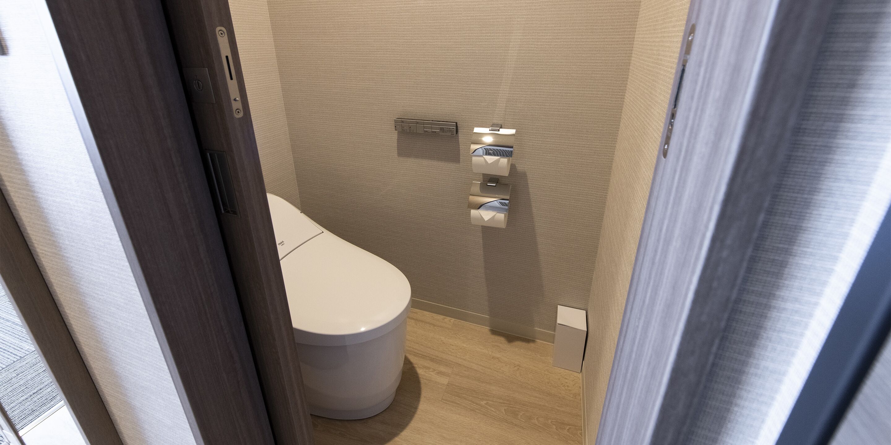 A compact bathroom with a toilet, a wall-mounted sink, and a towel dispenser.