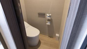 A compact bathroom with a toilet, a wall-mounted sink, and a towel dispenser.