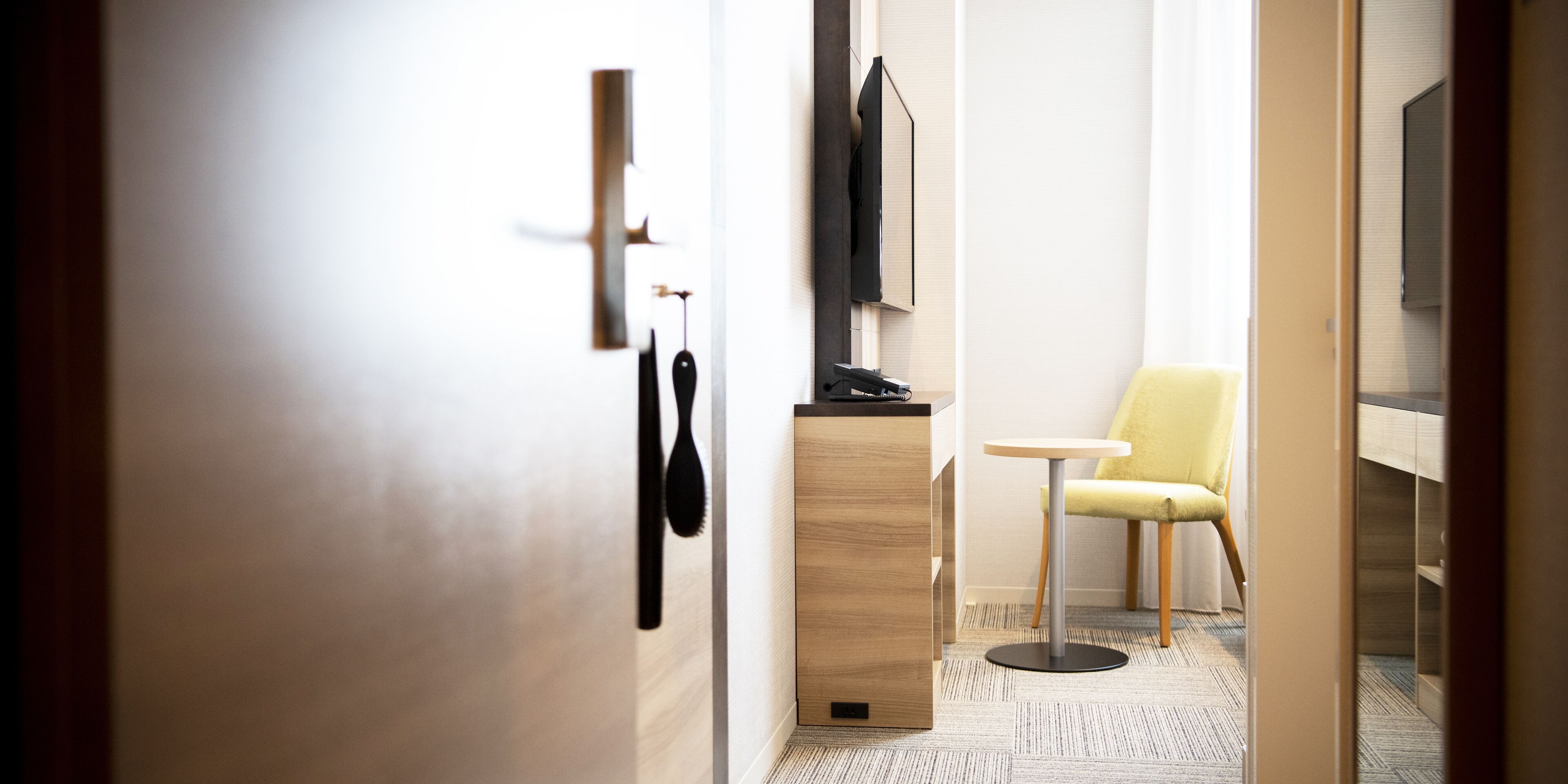 Ein Hotelzimmer mit einem Holztisch, einem Stuhl, einem Fernseher und einer Tür mit Griff.