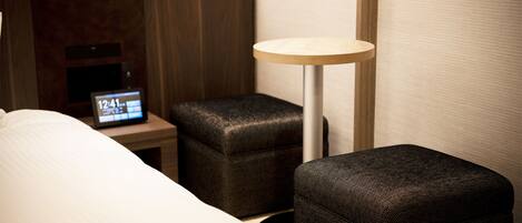 A hotel room with a bed, a bedside table with a clock, a small ottoman, and a floor lamp.