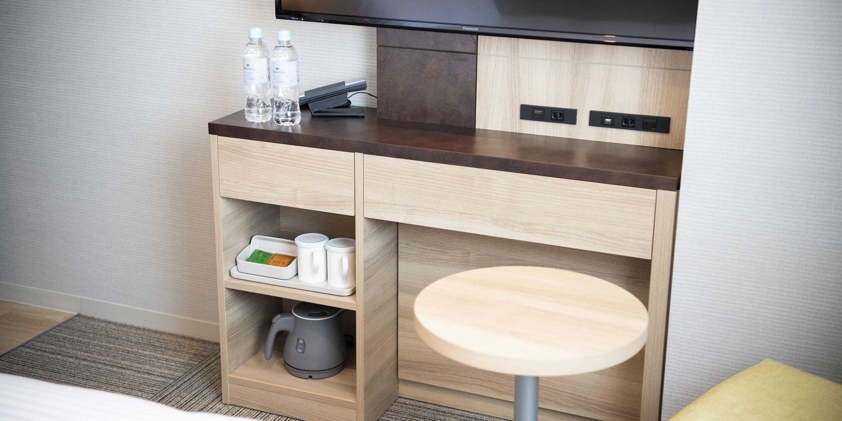 A hotel room with a wooden cabinet containing a kettle, mugs, and water bottles.