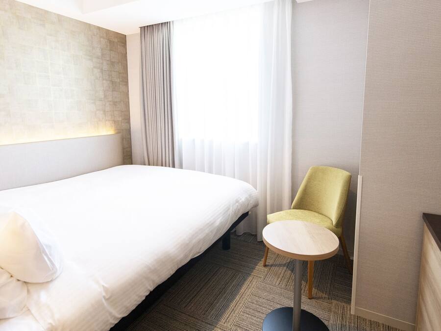 Una habitación de hotel con una cama, una mesita redonda pequeña, una silla y un televisor.