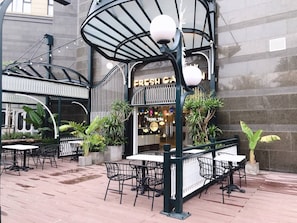 An outdoor café with tables and chairs, a sign reading "FRESH CA," and potted plants. - Bayhomes D' Le Roi Soleil Apartment (Hanoi)