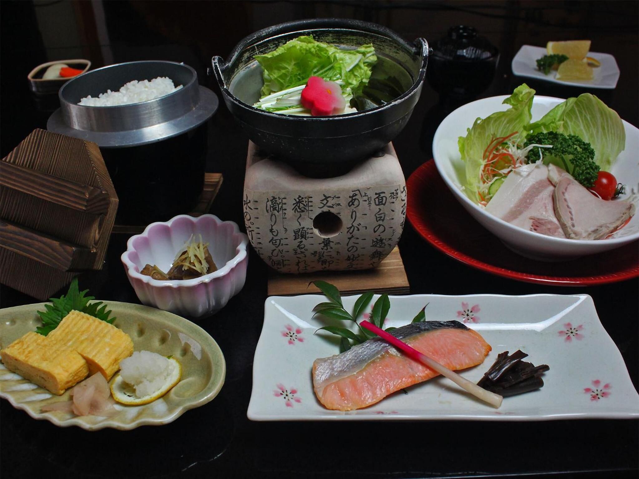 Una mesa con diferentes platos, entre ellos sushi, sashimi y una olla caliente.