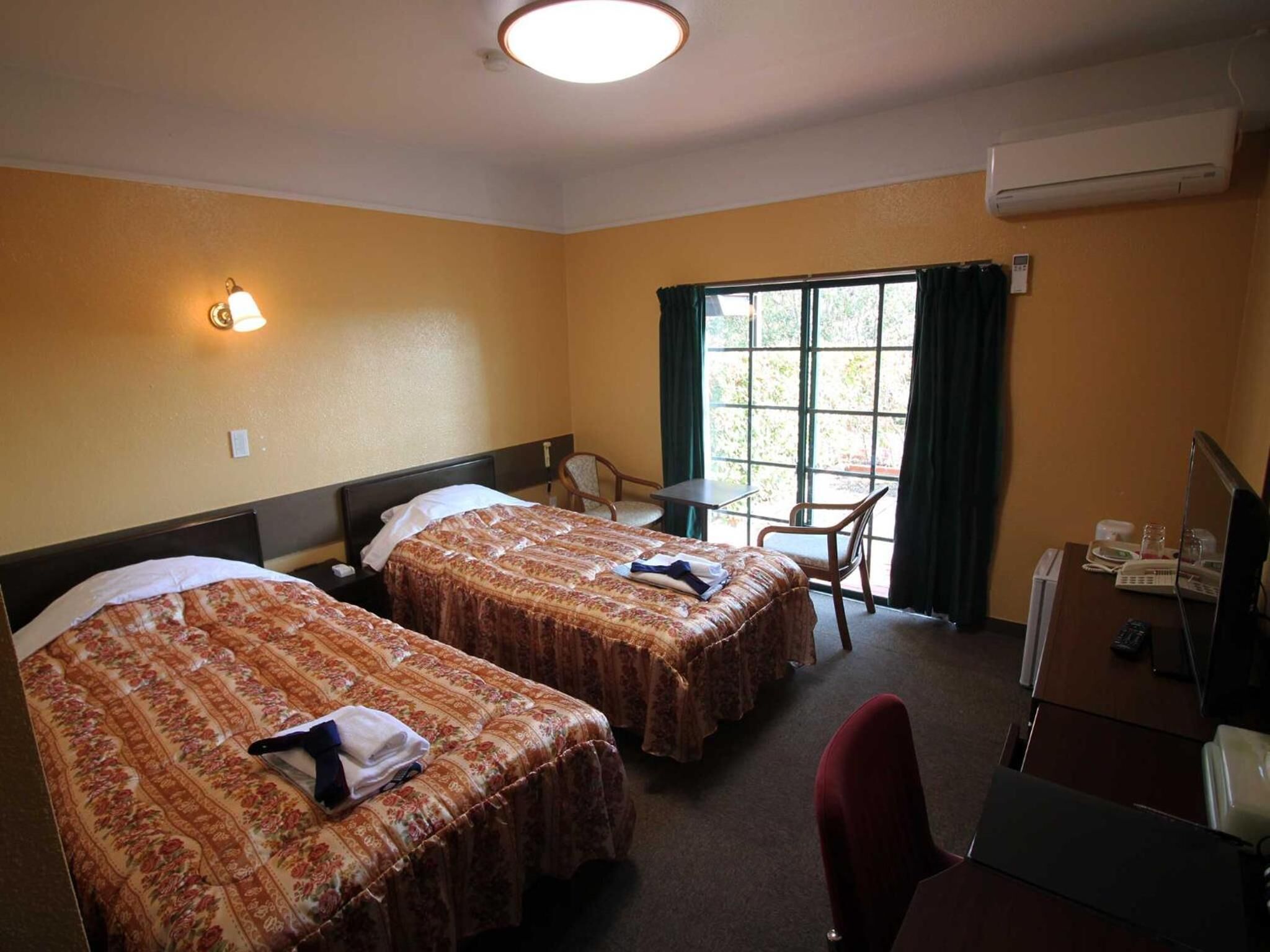 A hotel room with two beds, a desk, a chair, and a window with curtains.