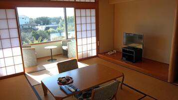 Ein traditioneller japanischer Raum mit Tatami-Boden, einem niedrigen Tisch mit Fernbedienung und einem Fernseher auf einem Ständer.