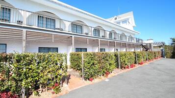 A modern building with a white facade, multiple balconies, and a well-maintained garden with various shrubs and flowers.