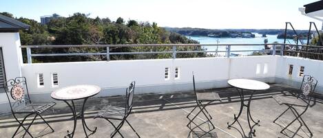 Terraza en la azotea con mobiliario exterior, incluyendo sillas metálicas y mesas redondas, con vistas panorámicas al agua y vegetación.
