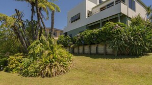 Een modern huis met twee verdiepingen, een plat dak, grote ramen en een verzorgde tuin met verschillende planten en een palmboom.