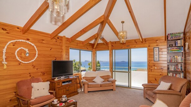 Een knus kamer in chaletstijl met een groot raam met uitzicht op de oceaan, houten wanden, een televisie en een boekenkast.