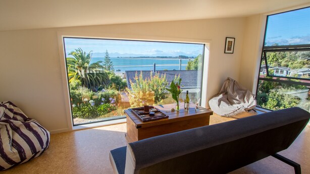 A modern living room with a large window offering a view of a beach and mountains.