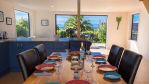 A dining area with a wooden table set for six, surrounded by dark blue cabinets and black leather chairs.