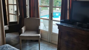 A room with a bed, a chair, a television, a wooden cabinet, and a sliding glass door leading to a pool area. - Villa with terraces and swimming pool panoramic view. Near golf courses and beach, 1km from village (Valbonne)