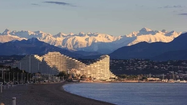 A coastal hotel with a modern architectural design, situated near a beach with a backdrop of snow-capped mountains. - Villa with terraces and swimming pool panoramic view. Near golf courses and beach, 1km from village (Valbonne)