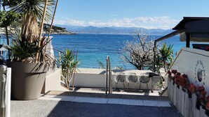 A coastal view with a paved walkway leading to a seating area with chairs and a table, overlooking the sea and mountains. - Villa with terraces and swimming pool panoramic view. Near golf courses and beach, 1km from village (Valbonne)