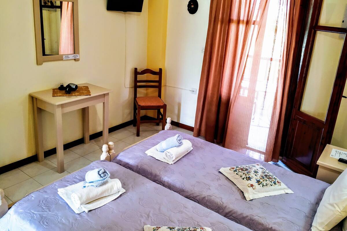 A hotel room with two beds, a desk, a chair, a television, and a window with curtains.