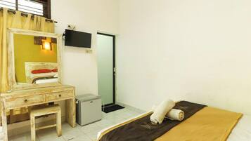 A room with a bed, a small desk with a mirror, a television mounted on the wall, and a door.