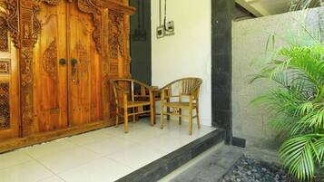 A wooden door with intricate carvings, a pair of wooden chairs, and a potted plant.