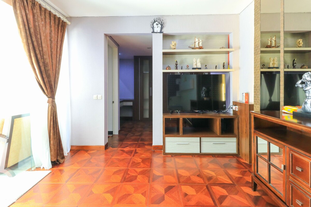 Una sala de estar con suelo de madera, un televisor sobre un mueble de madera y un aparador con objetos decorativos.