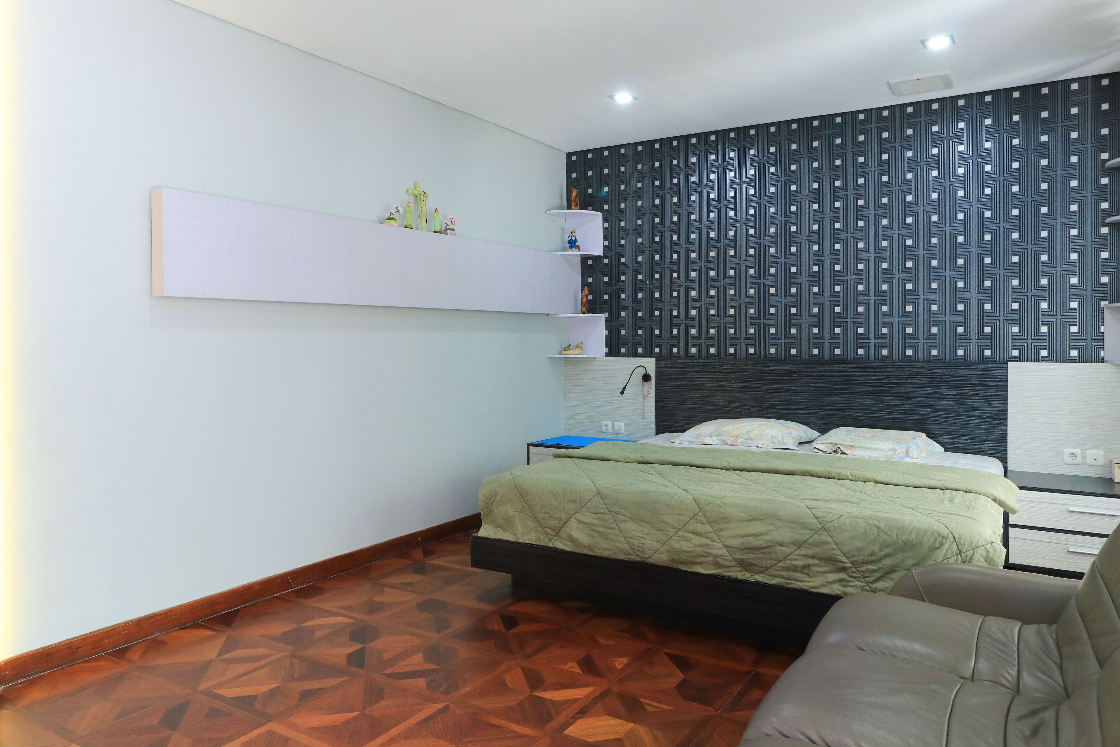 A bedroom with a bed, a sofa, a wall-mounted shelf, and a patterned wall.