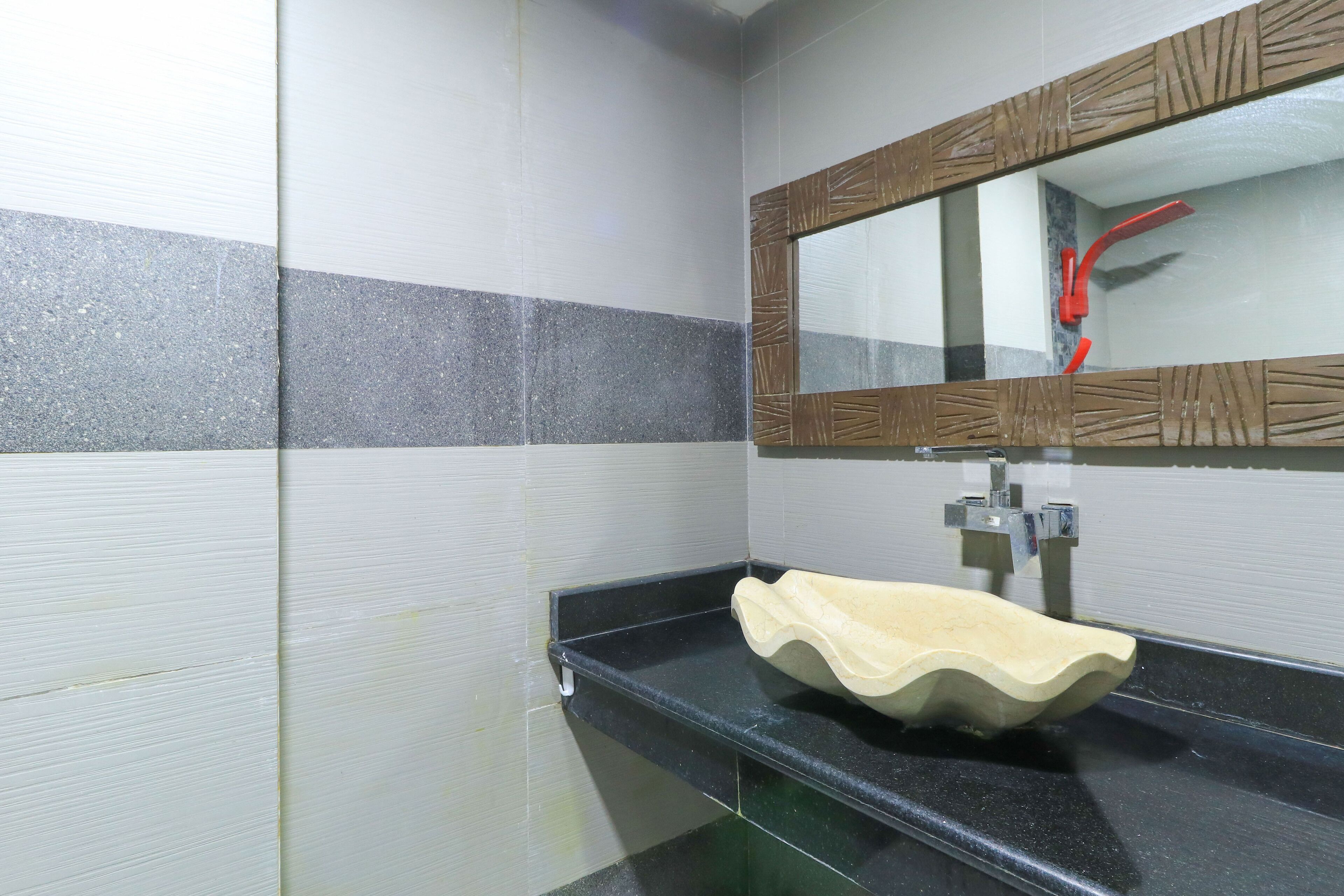 Un baño con mostrador negro, lavamanos color beige y espejo con marco de madera.