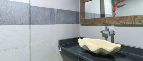 Un baño con mostrador negro, lavamanos color beige y espejo con marco de madera.