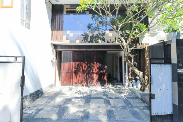 A modern building with a gated entrance, a tree in the foreground, and a clear sky. - Kubu Kalih Residence (Denpasar)