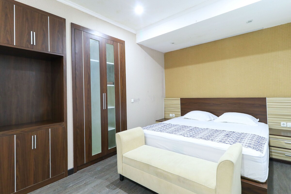 A hotel room with a bed, a wardrobe, a bench, and a headboard.