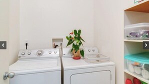 Zona de bugaderia amb dues rentadores, una planta en test i prestatges amb contenidors.