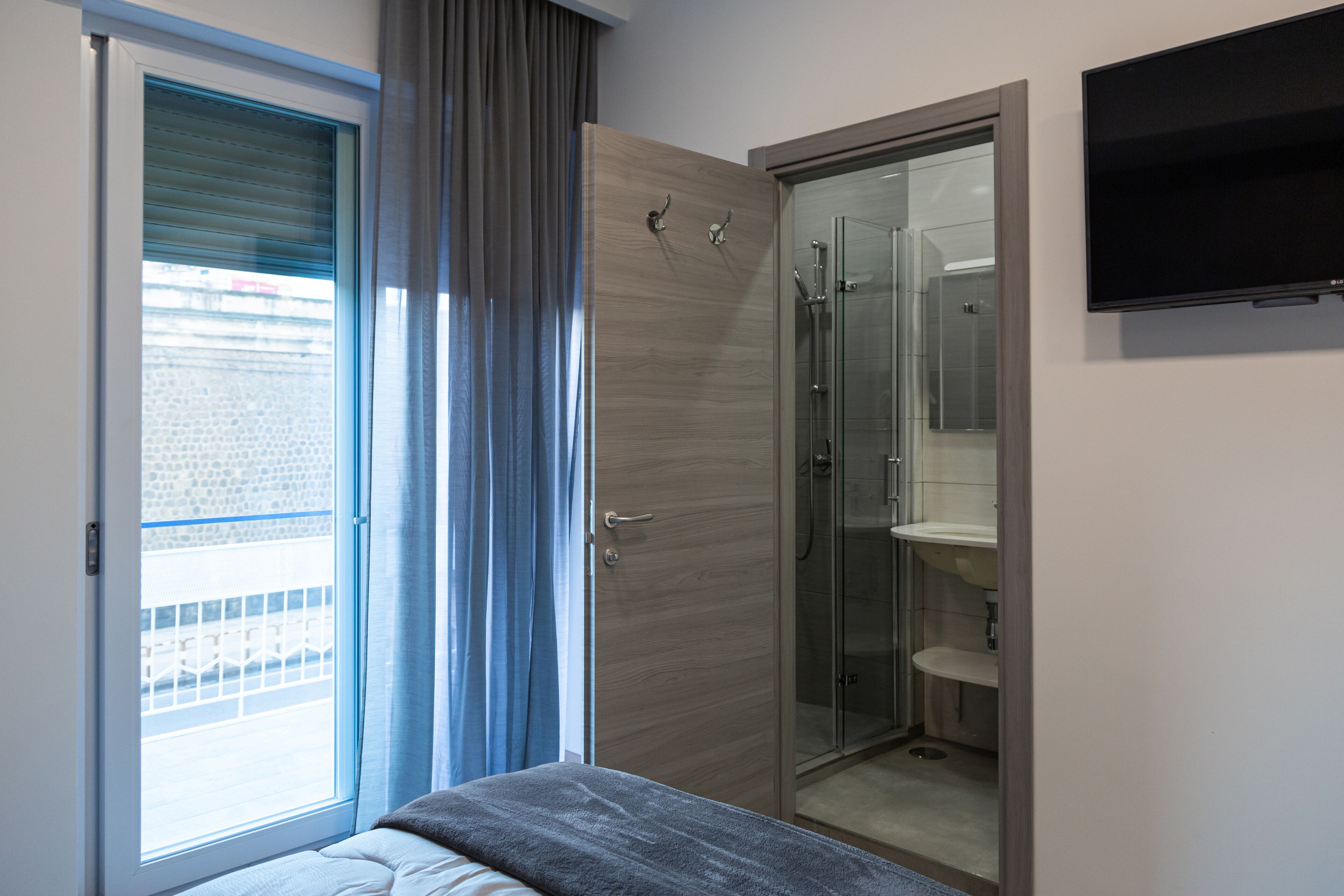 Ein modernes Schlafzimmer mit Bett, einer Schiebetür zum Balkon, einem begehbaren Kleiderschrank und einer Duschkabine.