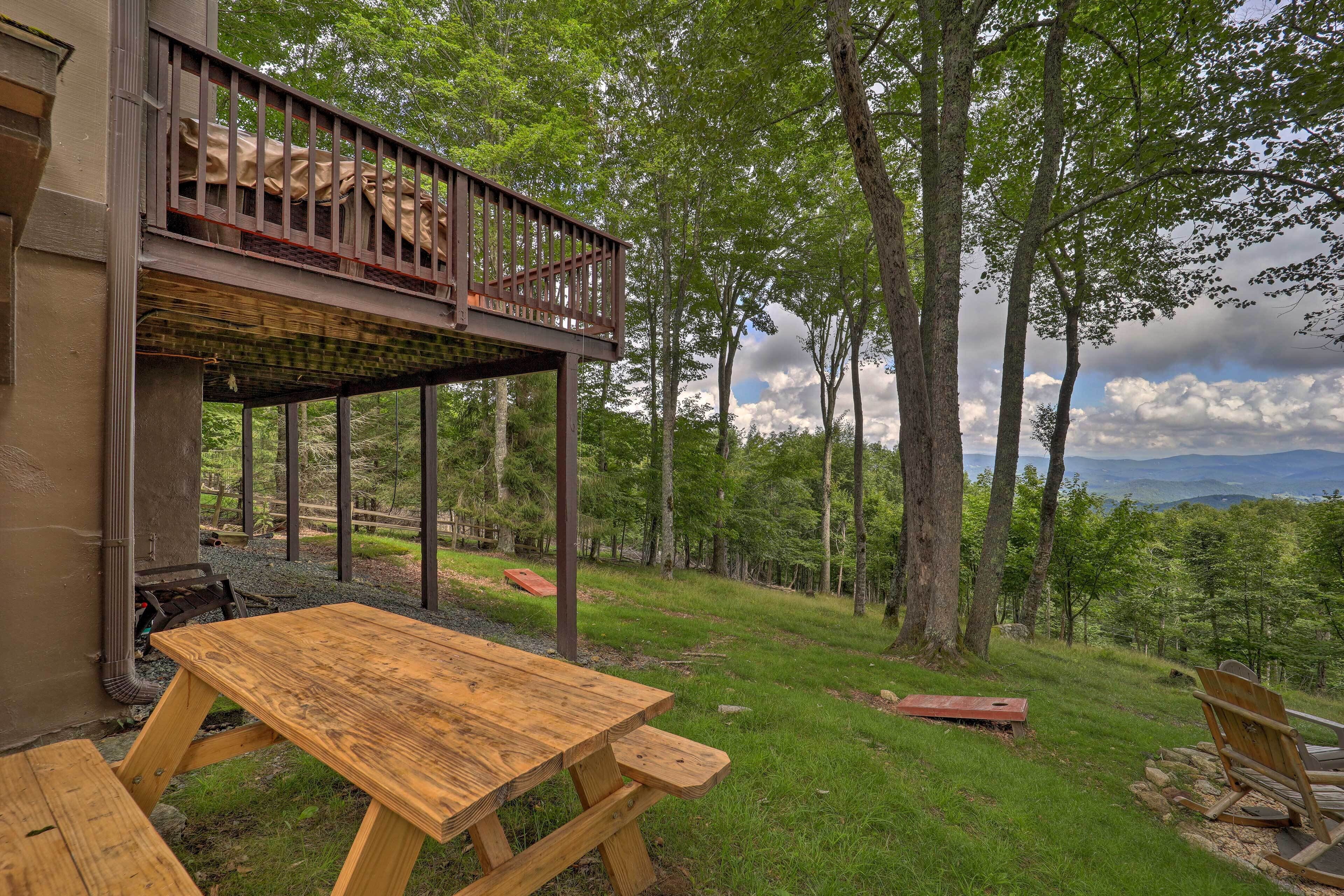 A wooden deck with a picnic table and chairs, overlooking a forested area with a view of distant mountains.