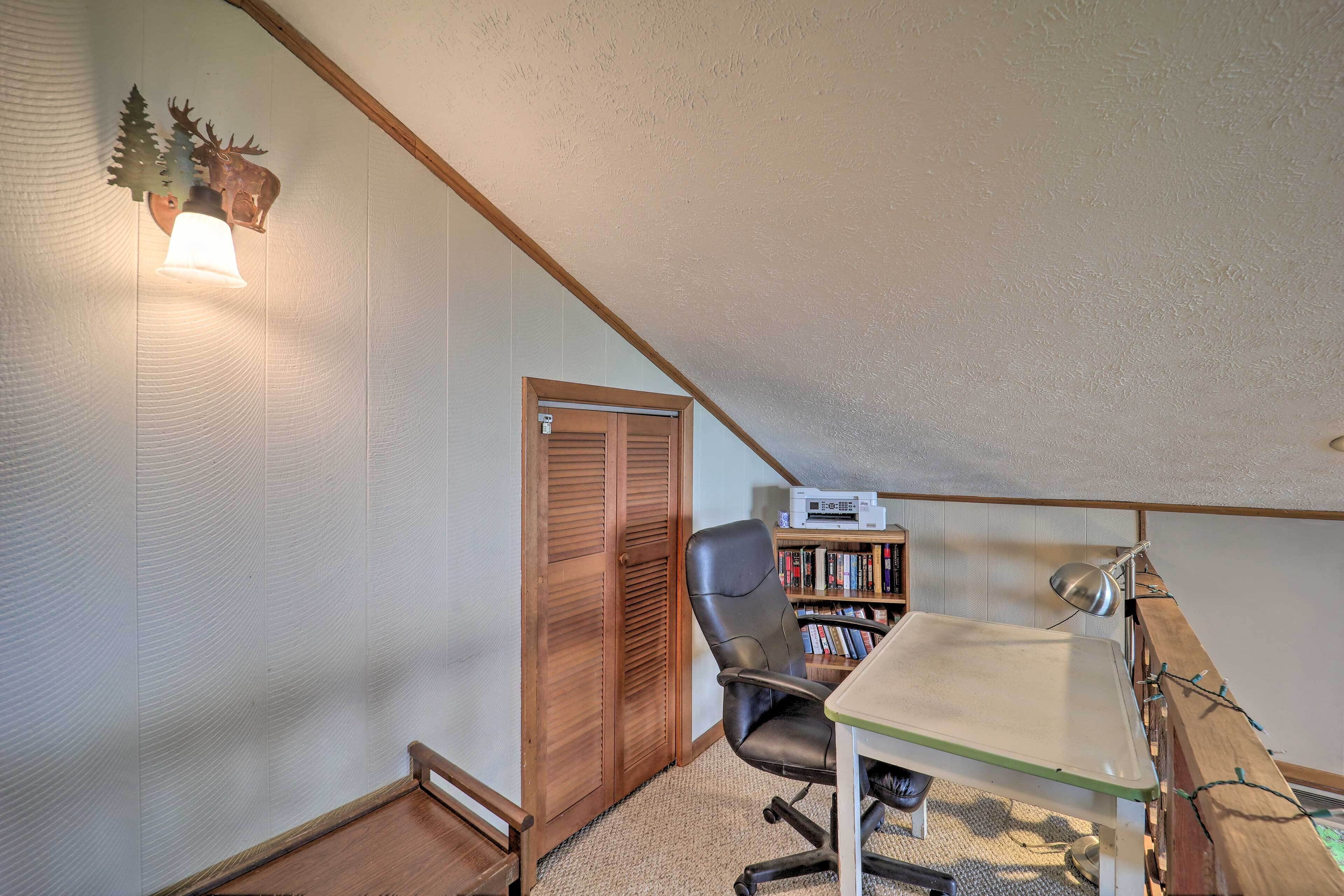 A small, well-lit attic room with a desk, chair, bookshelf, and a wooden door.