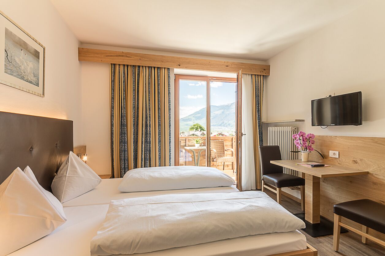Habitación de hotel con cama, escritorio, silla, televisión y vista a las montañas.