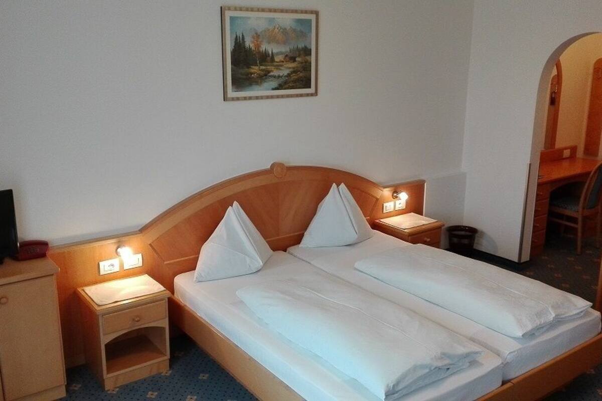 Una habitación de hotel con una cama, dos mesitas de noche, un televisor y un cuadro en la pared.