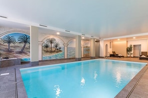 Ein Hallenbad mit Wandgemälden von Palmen und einer Strandlandschaft.