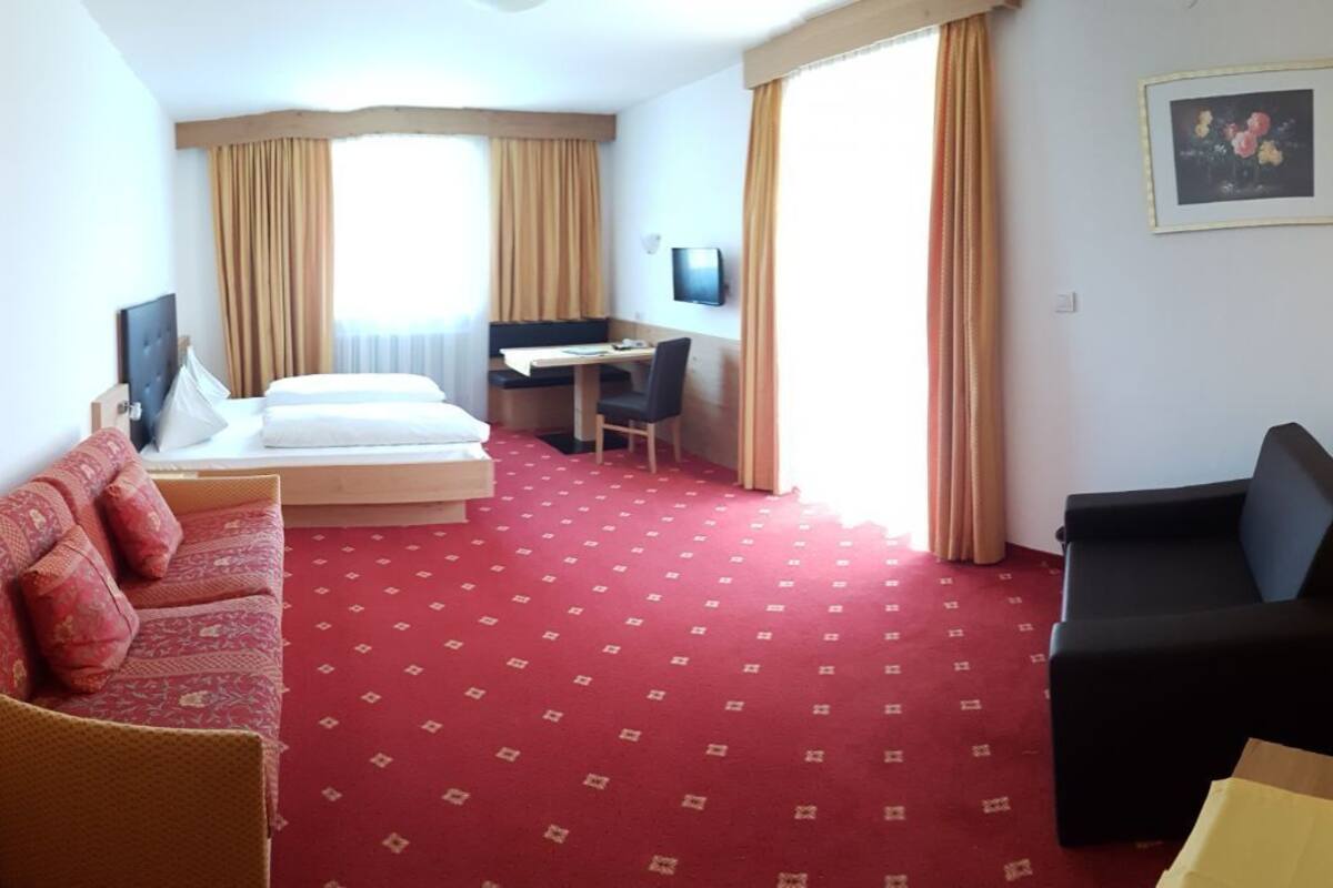 Habitación de hotel con cama, escritorio, silla, sofá y televisor.