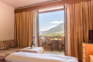 Ein Hotelzimmer mit Bett, einer Sitzecke, einem kleinen Tisch mit Pflanze und einem Balkon mit Tisch und Stühlen.